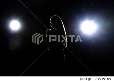 Silhouette of woman praying isolated on dark background in lanterns light Silhouette of woman praying isolated on dark background in lanterns light 73549169