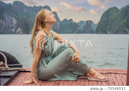 Attractive woman in a dress is traveling by boat in Halong Bay. Vietnam. Travel to Asia, happiness emotion, summer holiday concept. Picturesque sea landscape. Ha Long Bay, Vietnam Attractive woman in a dress is traveling by boat in Halong Bay. Vietnam. Travel to Asia, happiness emotion, summer holiday concept. Picturesque sea landscape. Ha Long Bay, Vietnam 73549532