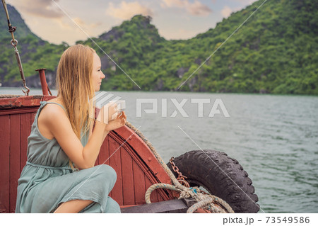 Attractive woman in a dress is drinking coffee, traveling by boat in Halong Bay. Vietnam. Travel to Asia, happiness emotion, summer holiday concept. Picturesque sea landscape. Ha Long Bay, Vietnam 73549586
