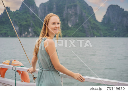 Attractive woman in a dress is traveling by boat in Halong Bay. Vietnam. Travel to Asia, happiness emotion, summer holiday concept. Picturesque sea landscape. Ha Long Bay, Vietnam Attractive woman in a dress is traveling by boat in Halong Bay. Vietnam. Travel to Asia, happiness emotion, summer holiday concept. Picturesque sea landscape. Ha Long Bay, Vietnam 73549620