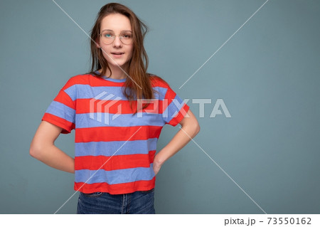 Pretty shy young female student standing isolated over blue background wall keeping hands behind 73550162