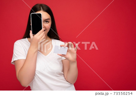 Photo of attractive happy young brunette lady wearing casual white t-shirt isolated over red Photo of attractive happy young brunette lady wearing casual white t-shirt isolated over red 73550254