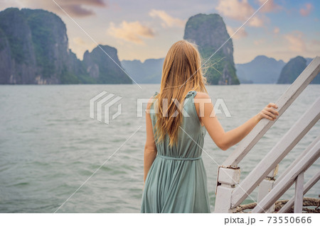 Attractive woman in a dress is traveling by boat in Halong Bay. Vietnam. Travel to Asia, happiness emotion, summer holiday concept. Picturesque sea landscape. Ha Long Bay, Vietnam Attractive woman in a dress is traveling by boat in Halong Bay. Vietnam. Travel to Asia, happiness emotion, summer holiday concept. Picturesque sea landscape. Ha Long Bay, Vietnam 73550666