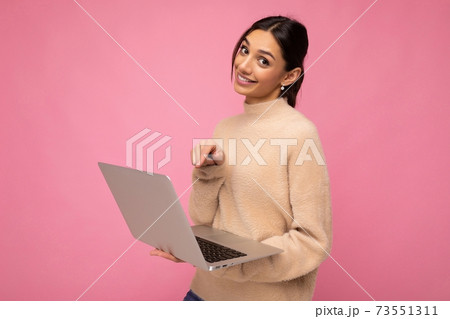 Photo of Beautiful young brunette woman wearing beige sweater holding netbook computer looking at Photo of Beautiful young brunette woman wearing beige sweater holding netbook computer looking at 73551311