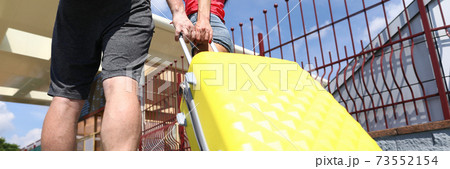 Man and woman carry yellow suitcase on platform. 73552154