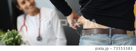 Man demonstrates cellulite on his sides to doctor. 73553383