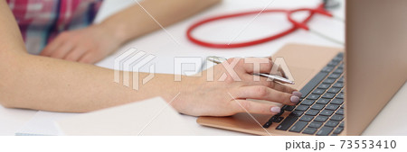 Female hands are working on laptop next to stethoscope. 73553410
