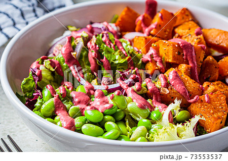 Vegan salad bowl with baked sweet potato, edamame beans, nuts and pink beetroot dressing. Vegan food concept. Vegan salad bowl with baked sweet potato, edamame beans, nuts and pink beetroot dressing. Vegan food concept. 73553537