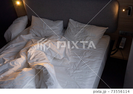 Unmade bed in an hotel room. 73556114