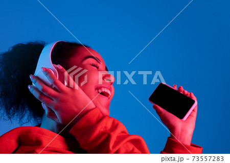 African-american woman's portrait isolated on blue studio background in multicolored neon light African-american woman's portrait isolated on blue studio background in multicolored neon light 73557283
