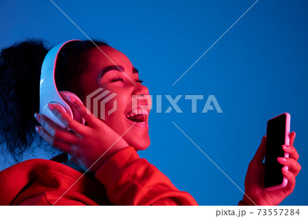 African-american woman's portrait isolated on blue studio background in multicolored neon light African-american woman's portrait isolated on blue studio background in multicolored neon light 73557284