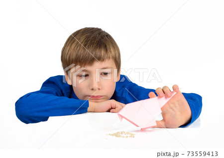 Origami: a schoolboy boy in a blue T-shirt sits at the table and plays with a paper bird, wants to feed her 73559413