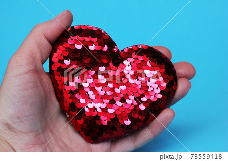 Red sparkling heart with sequins in hand on a blue background. T Red sparkling heart with sequins in hand on a blue background. T 73559418