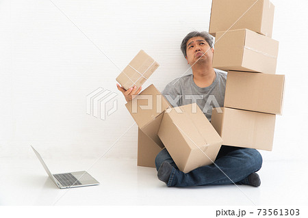 Asian Shopaholic sitting on the floor in the living room and Cardboard Box on top of him after The courier delivered to the home. Concept of shopping online and Shopaholic. Asian Shopaholic sitting on the floor in the living room and Cardboard Box on top of him after The courier delivered to the home. Concept of shopping online and Shopaholic. 73561303