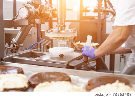 The pastry chef makes cake using modern equipment for the production of cakes. Line for spreading cream on cake, biscuit The pastry chef makes cake using modern equipment for the production of cakes. Line for spreading cream on cake, biscuit 73562408