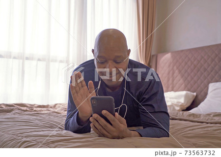 Happy smiling business, black man, African American people talking on the phone to colleagues in webcam video call conference in quarantine on bed in bedroom at home in morning. Lifestyle 73563732