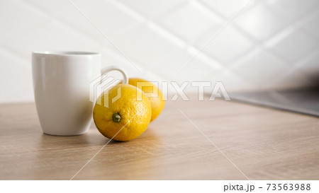 Two lemons on the kitchen table near a white mug of tea Two lemons on the kitchen table near a white mug of tea 73563988