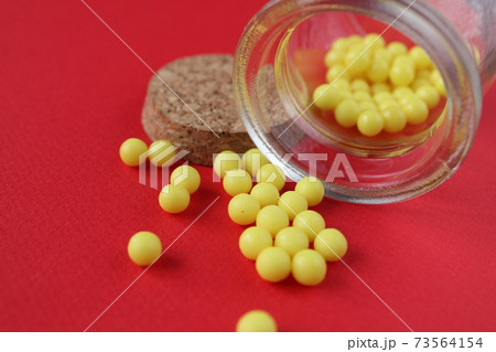 Vitamins homeopathy tablets are sucked out of the packaging jar on a red background with a copyspace close-up Vitamins homeopathy tablets are sucked out of the packaging jar on a red background with a copyspace close-up 73564154