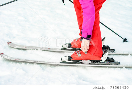 skis, boots and sticks in red on woman's leg close up. 73565430