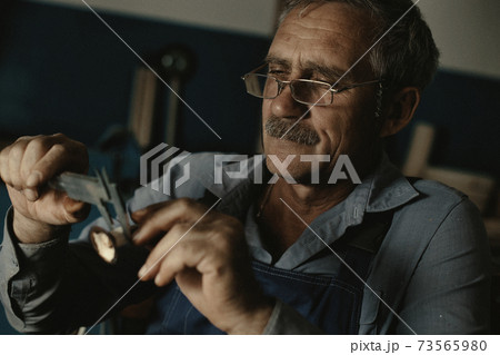 An old master with glasses works in a workshop 73565980