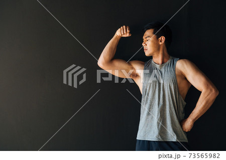 Focused young ethnic sportsman demonstrating biceps in studio 73565982