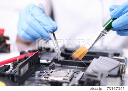 Gloved handyman with brush and tweezers repairs motherboard Gloved handyman with brush and tweezers repairs motherboard 73567305