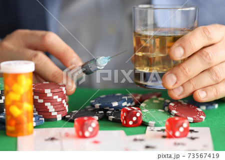 Male hands are holding syringe with needle and glass with alcohol next to casino chips 73567419