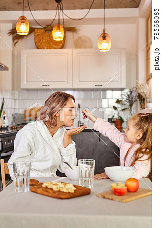 young caucasian woman and child girl have breakfast in the kitchen at home 73568085