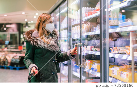 Woman at supermarket freezer section wearing face mask Woman at supermarket freezer section wearing face mask 73568160