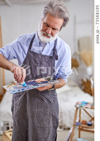 senior grey haired artist man painting using painter palette 73568195