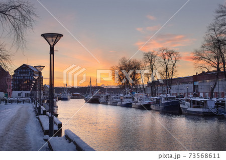 Klaipeda city, Lithuania in January. An old town, river and boats covered by winter snow, cold weather, empty streets. Orange and yellow cloudy sunset sky 73568611