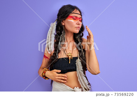 portrait of shamanic female with Indian feather on hair and colourful painted make-up portrait of shamanic female with Indian feather on hair and colourful painted make-up 73569220