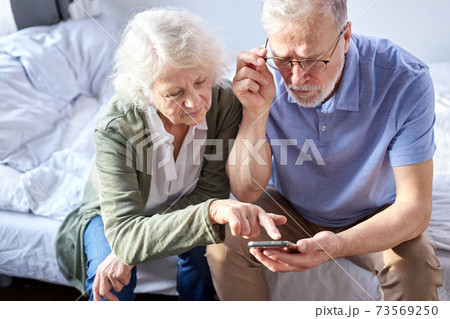 elderly senior couple looking at children's photos in smartphone elderly senior couple looking at children's photos in smartphone 73569250