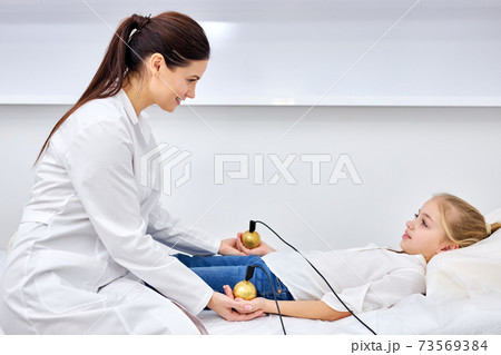 young caucasian female doctor therapist treating child girl using electrical stimulator while young caucasian female doctor therapist treating child girl using electrical stimulator while 73569384