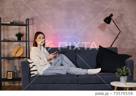 Young asian woman sitting on a sofa in a cozy room looks at the camera Young asian woman sitting on a sofa in a cozy room looks at the camera 73570559