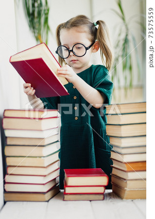 Little cute kid girl in glasses with pile of books, vertical 73575559