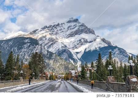 Banff Avenue in snowy autumn sunny day. Snow-covered Cascade Mountain with blue sky and white clouds in the background. Banff National Park, Canadian Rockies. 73579181