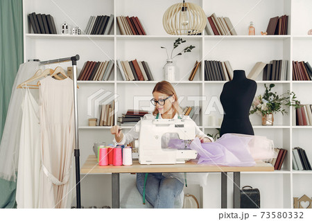 Woman sitting in studio and sew cloth Woman sitting in studio and sew cloth 73580332