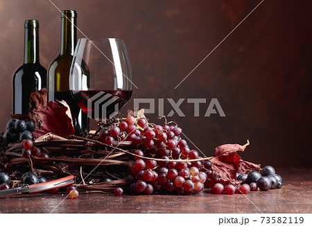 Red wine and fresh grapes with dried up vine leaves. 73582119