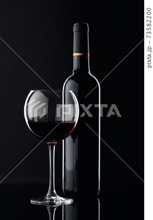 Bottle and glass of red wine on a black background. 73582200