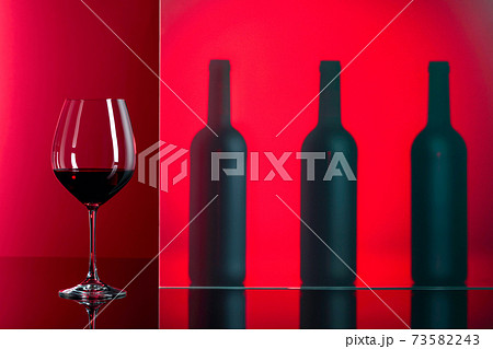 Bottles and glass of red wine on a red background. Bottles and glass of red wine on a red background. 73582243