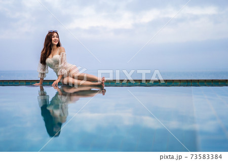 woman sitting on edge of swimming pool and looking to the sea 73583384