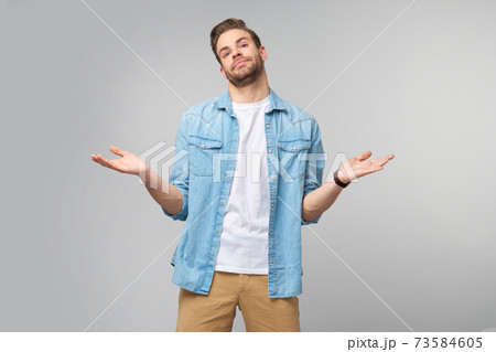 Portrait of confused clueless young man in jeans shirt standing over grey background 73584605