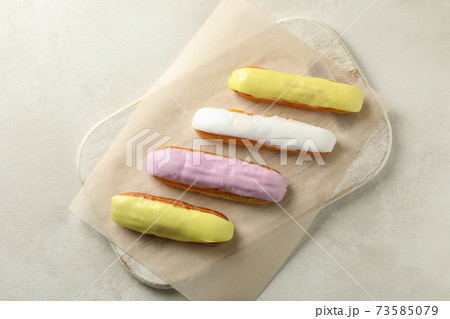 Board with eclairs with custard on white textured background 73585079