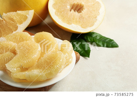 Ripe pomelo and plate with pomelo slices on white textured background 73585275