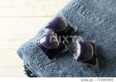 Towel with laundry capsules on white wooden background, close up 73585989