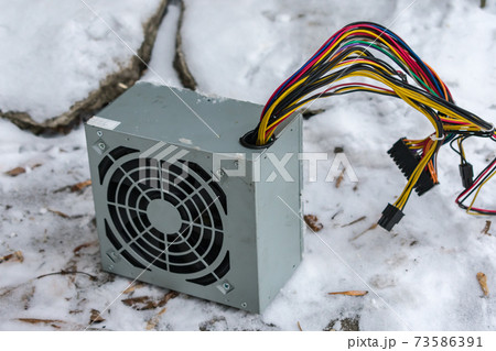 The PC power supply lies at an electronics dump in winter in the snow 73586391