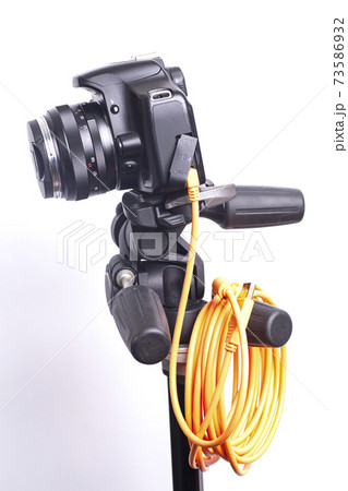Digital photo camera on black tripod with orange rolled cable 73586932