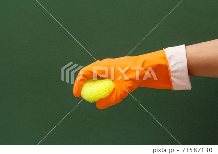 Woman's hand in protective glove with sponge on the green background. 73587130