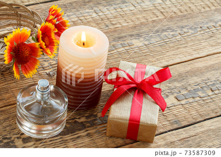 Perfume, gift box, candle and fresh flowers on wooden table. 73587309